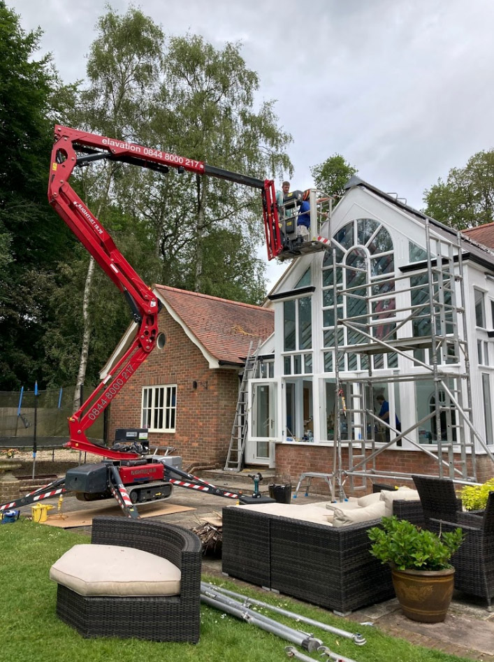wooden conservatory being painted by man in cherry picker crane crane